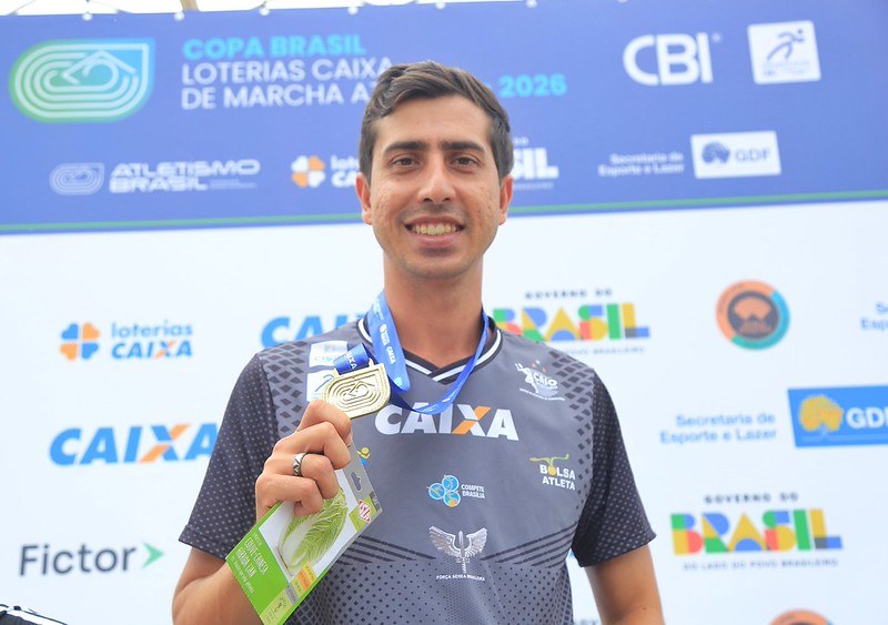 O atleta Caio Bonfim sorri enquanto segura a medalha de ouro.