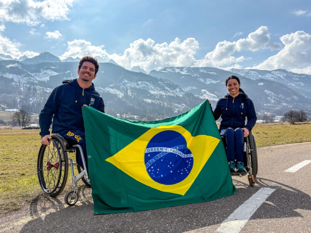 Esquiadores Cristian Ribera e Aline Rocha seguram a bandeira do Brasil em Predazzo, na Itália