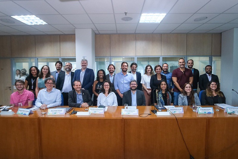 Participantes do GTI posam para foto atrás da mesa de reunião.