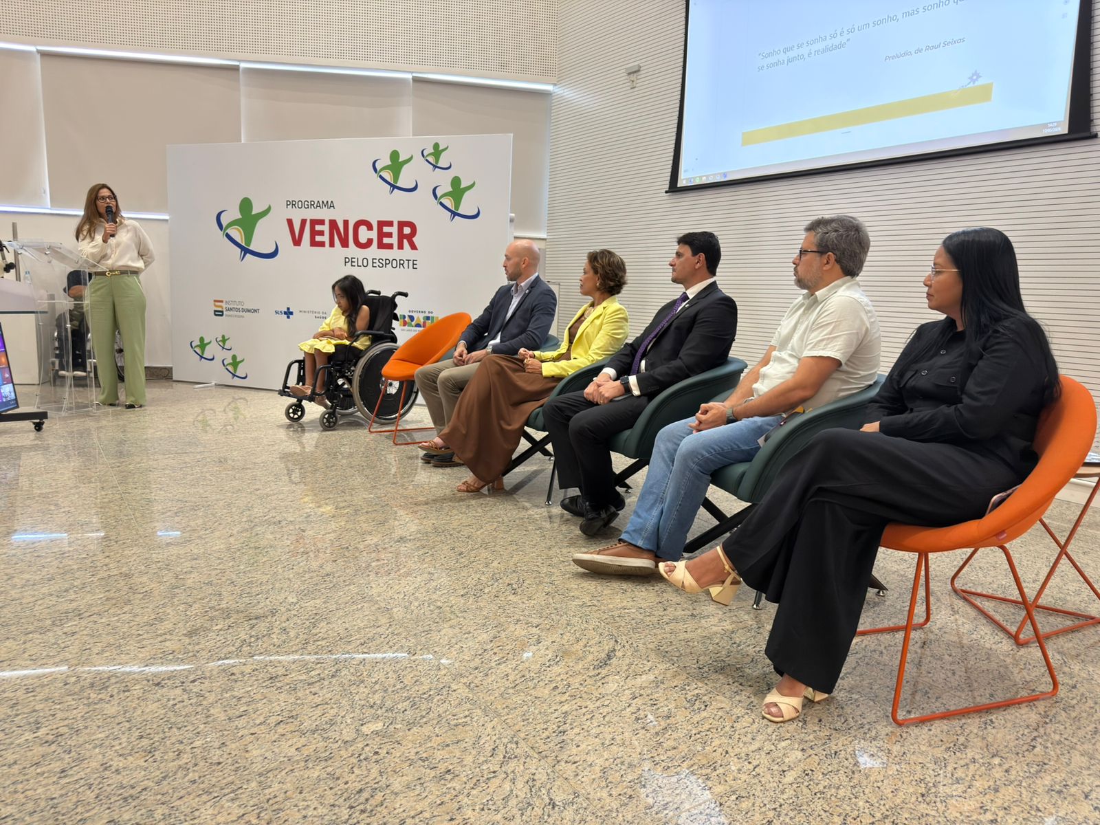 Uma mulher apresenta enquanto, sentados, os demais assistem.