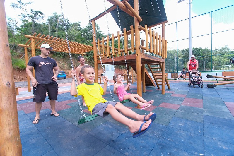Crianças jogam futebol no campo com grama sintética.