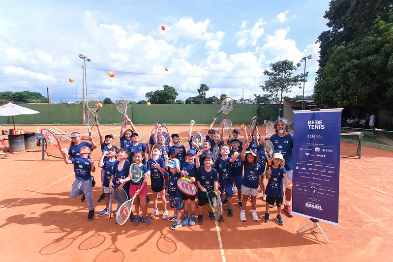 Crianças com as raquetes sorriem e  professor acompanha.