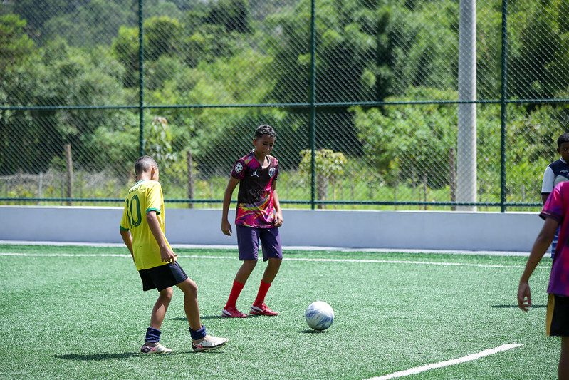 3 meninos jogam futebol em campo de grama sintética