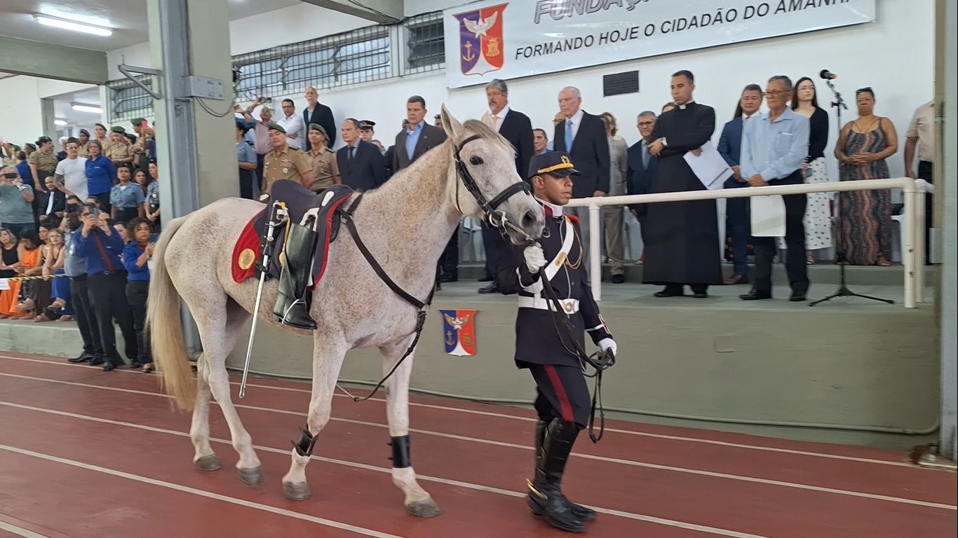Militar conduz cavalo durante cerimônia da Fundação Osorio em ginásio escolar.