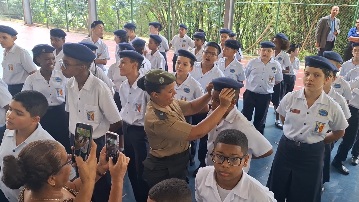 Militar ajusta boina de estudante durante cerimônia escolar com familiares presentes.