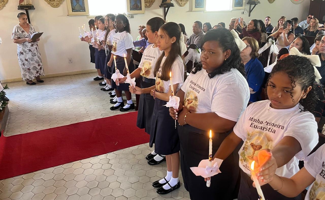 Crianças em fila seguram velas acesas durante cerimônia religiosa em igreja.