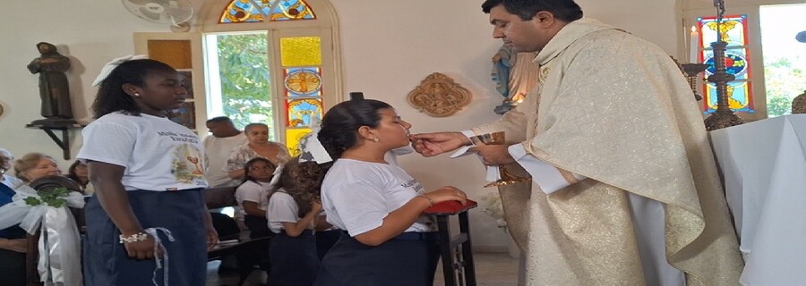 Padre distribui hóstia a criança durante celebração da Primeira Eucaristia.