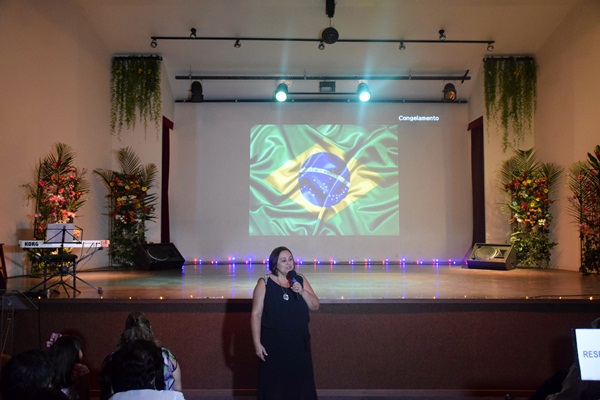 Mulher cantando no palco com a bandeira do Brasil projetada ao fundo.
