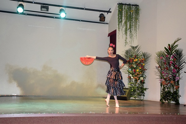 Bailarina se apresentando sozinha no palco com vestido flamenco e leque vermelho.