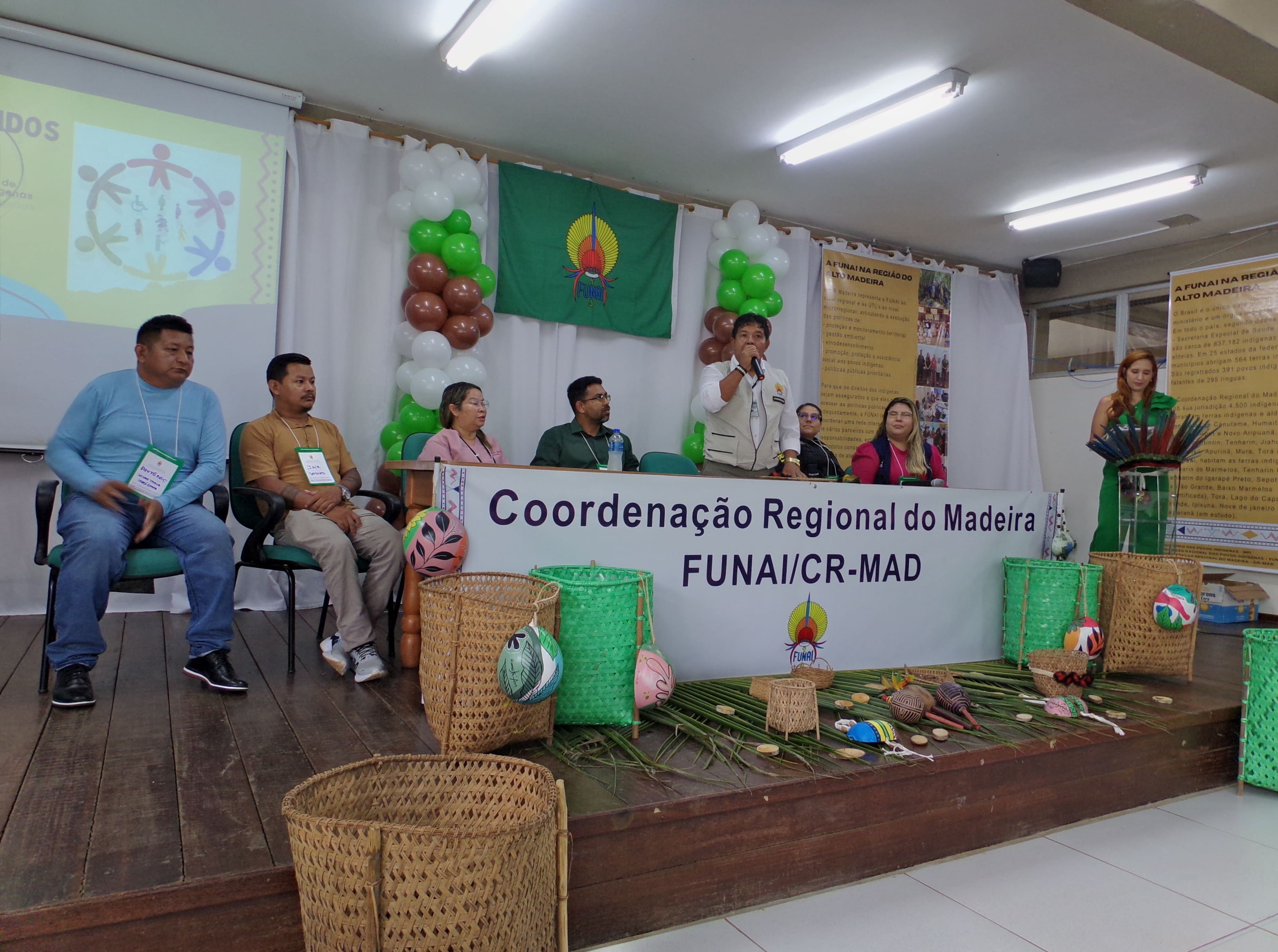 Mesa de evento da FUNAI com participantes e artesanato indígena exposto no palco.