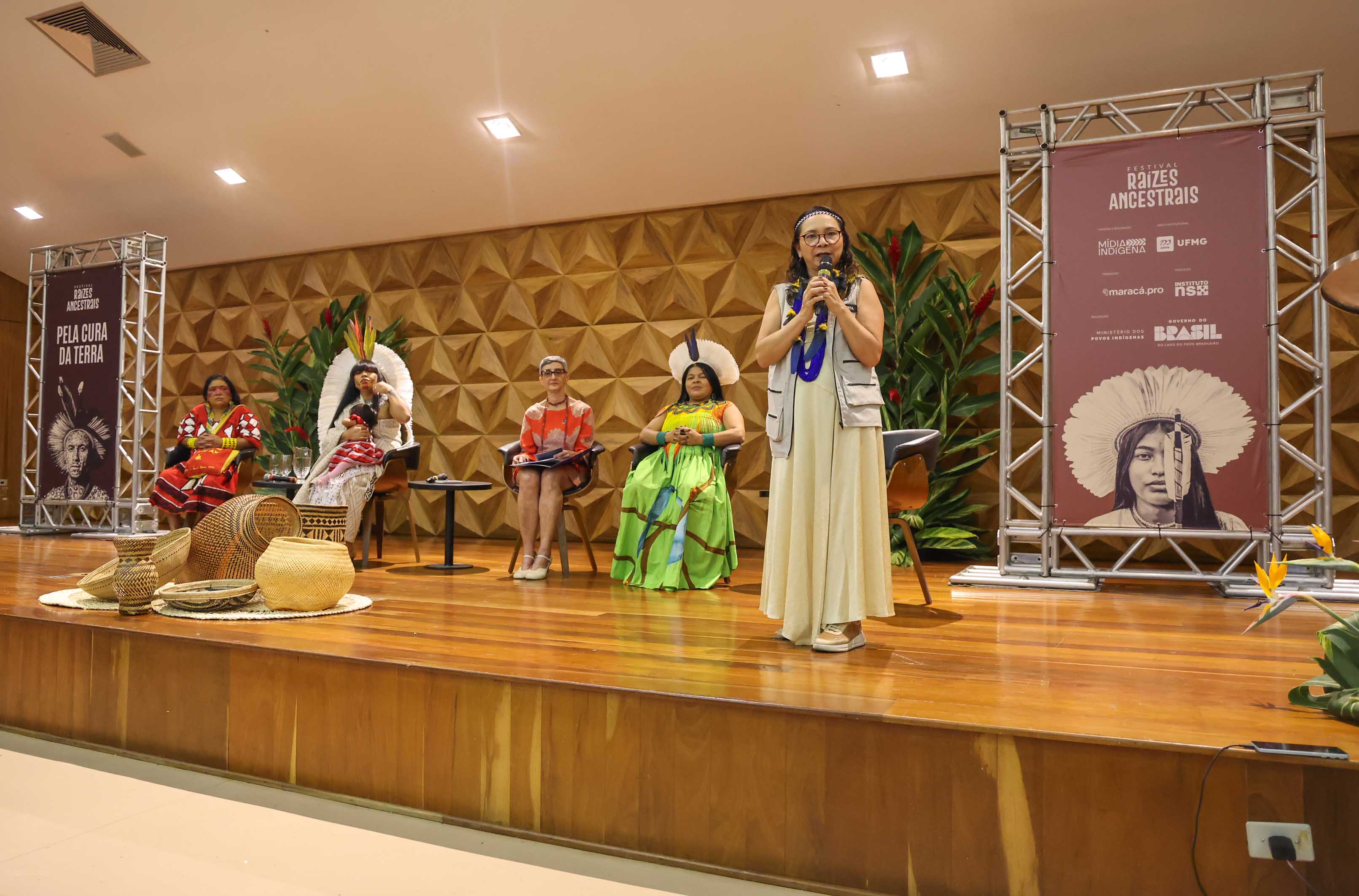 5 mulheres em um palco, presidenta da Funai com microfone falando