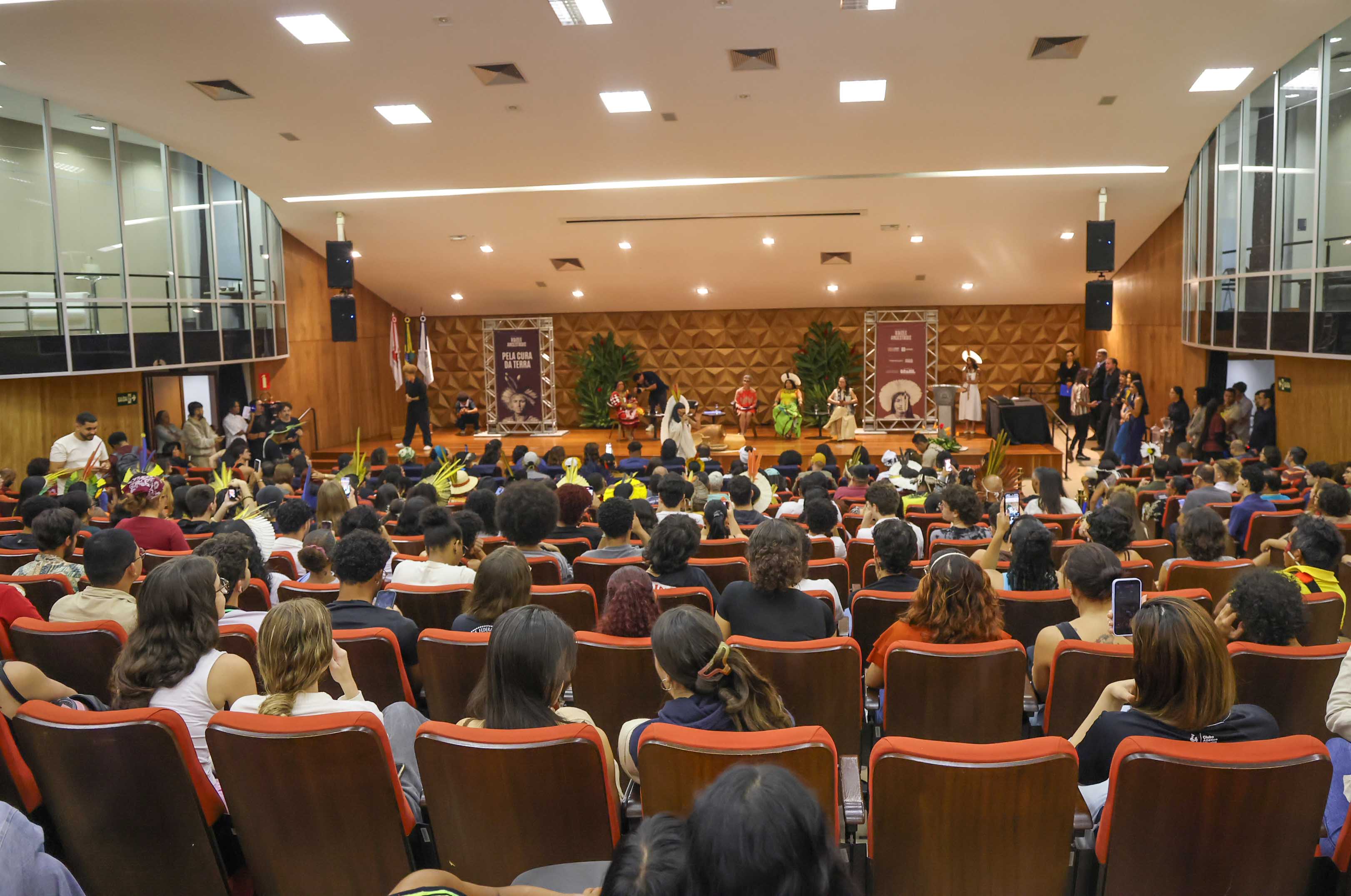 auditório com várias pessoas sentadas e um palco ao fundo