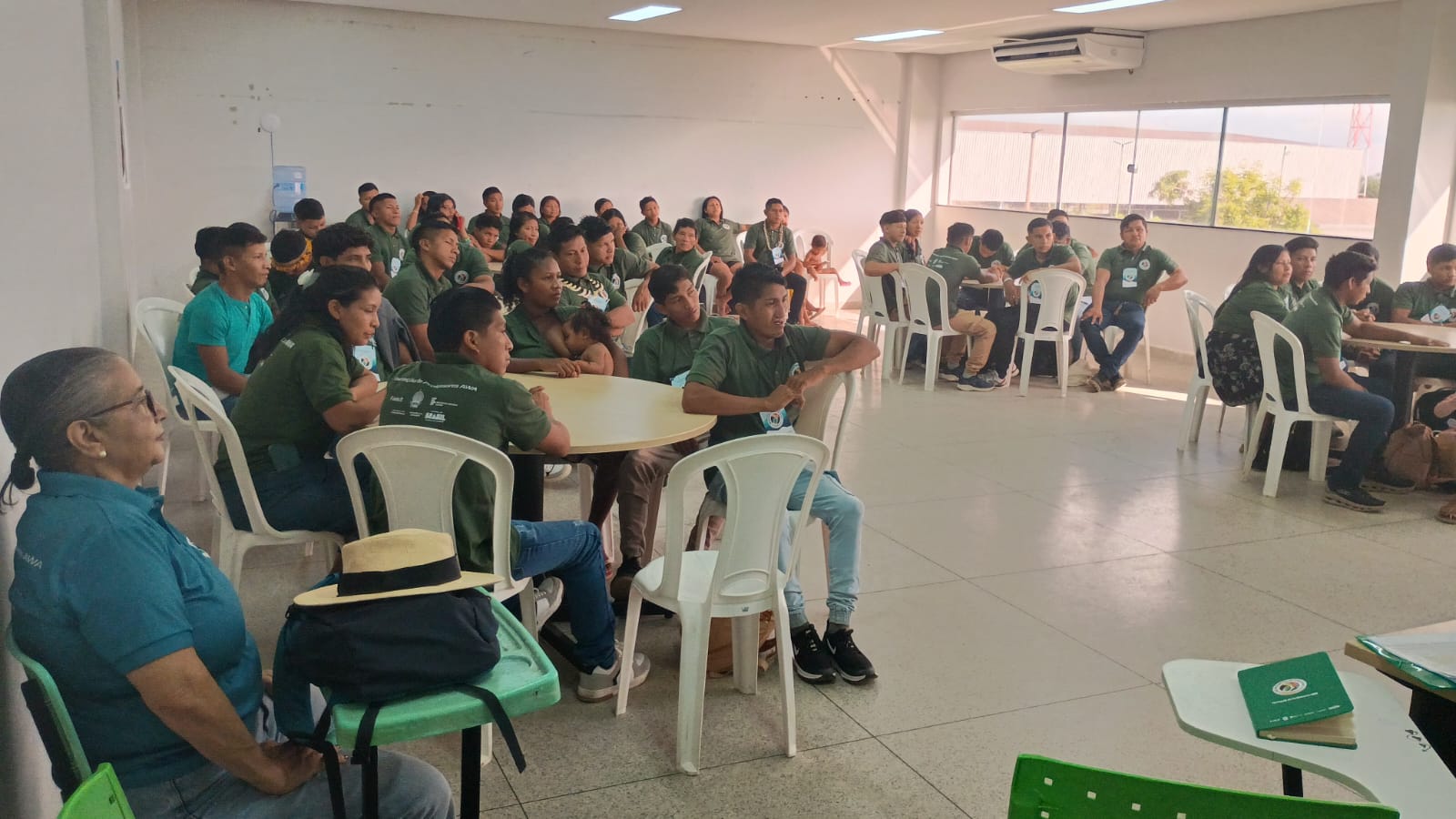 Indígenas sentados em cadeira branca assitindo uma aula do magistério indígena