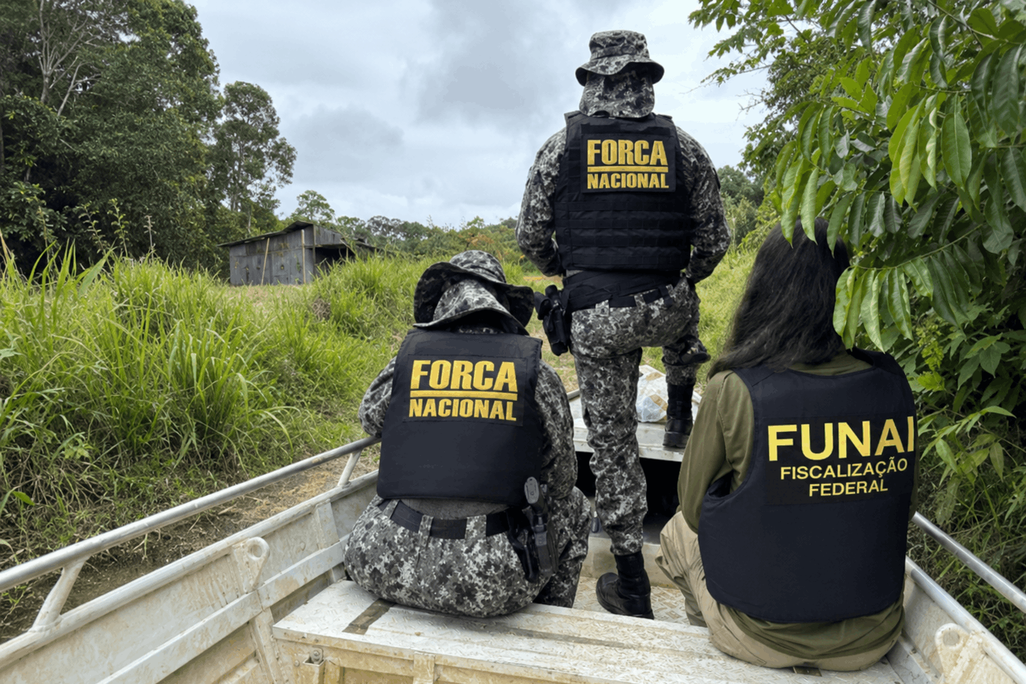 Servidores da Funai e Força Nacional dentro de barco, de costas