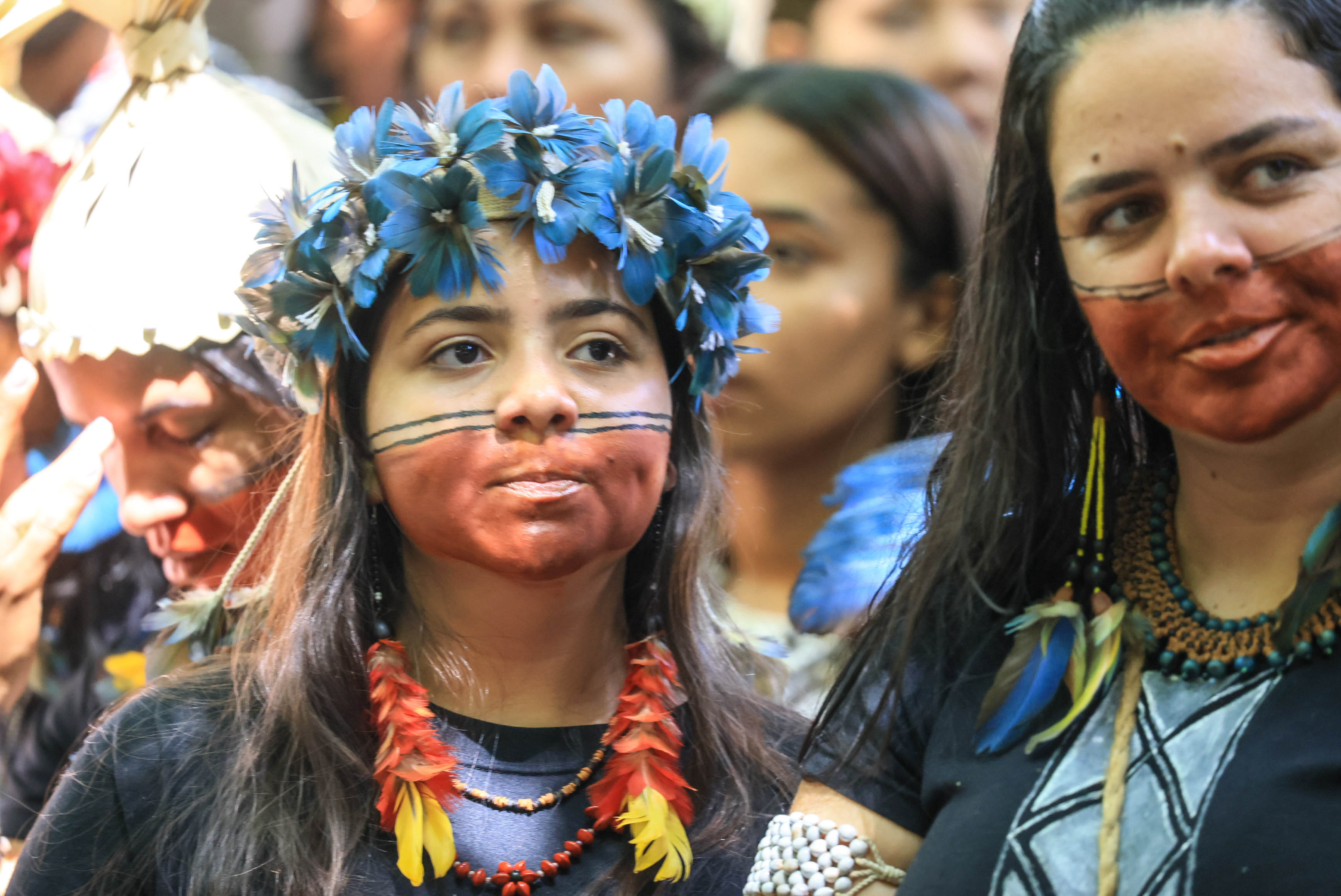 Mulheres indígenas Xukuru usando acessórios tradicionais, coroa de flores e pinturas faciais.