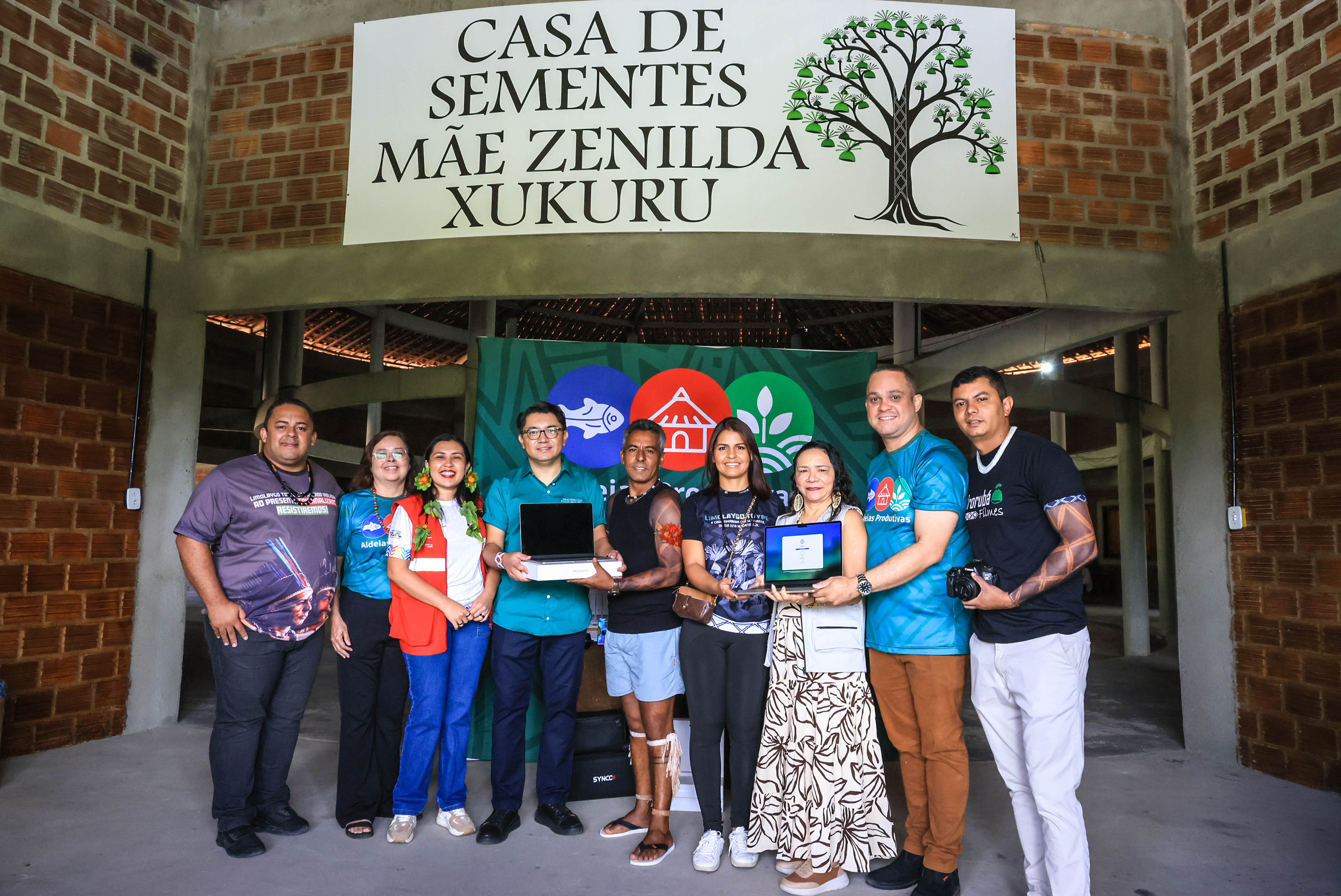 Colaboradores do projeto posam abaixo da placa "Casa de Sementes Mãe Zenilda Xukuru"