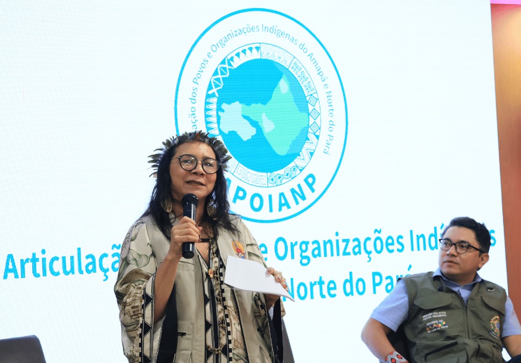 Presidenta da Funai falando no palco com microfone na mão.