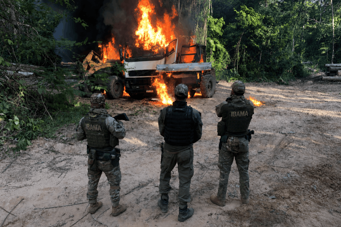 Homens de costas vedo maquinário sendo incendiado