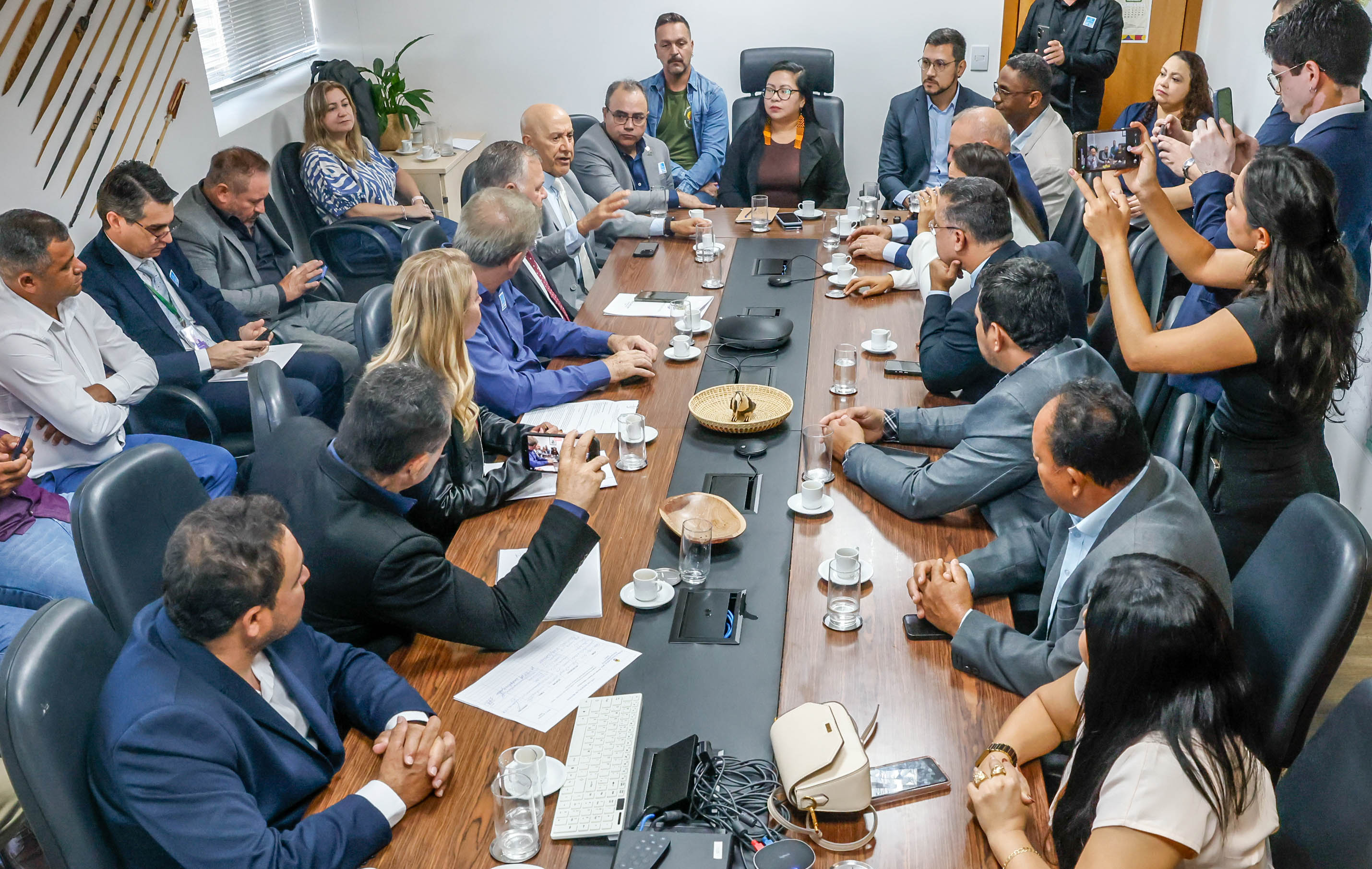 Muitas pessoas em reunião ao redor de uma mesa, algumas pessoas em pé