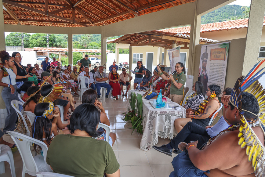 Reunião em espaço coberto com pessoas sentadas em círculo e fala conduzida ao centro.