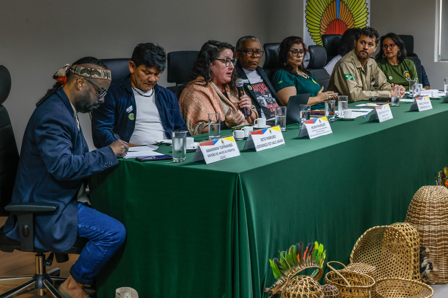 Foto de mesa de debate com sete participantes, um deles fala ao microfone.
