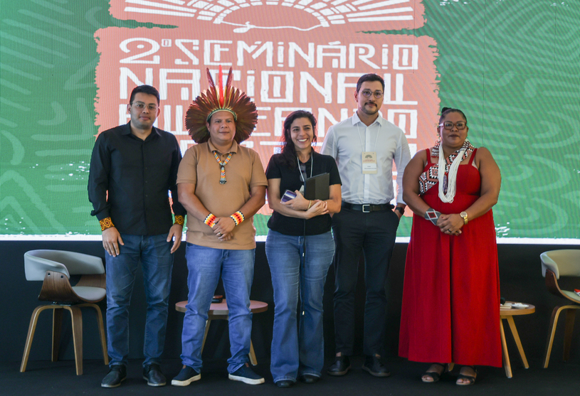 Representantes de organizações indígenas e órgãos indigenistas posam para foto no palco do seminário