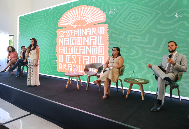 Presidenta da Funai, ao centro, entre representantes de órgãos indigenistas, fala ao microfone.