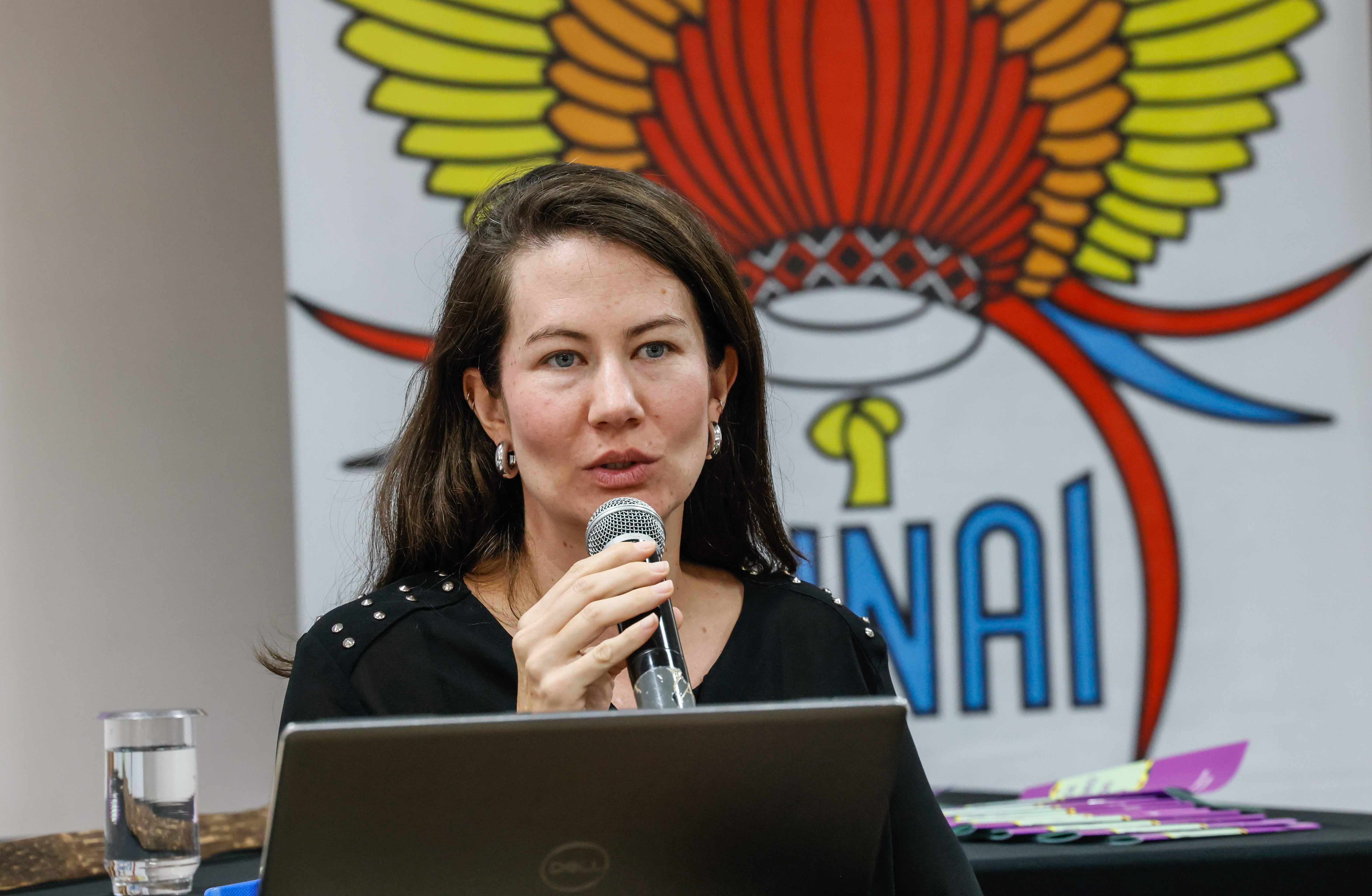 Representante da CGU discursa em evento, segura um microfone, ao fundo há um banner da Funai