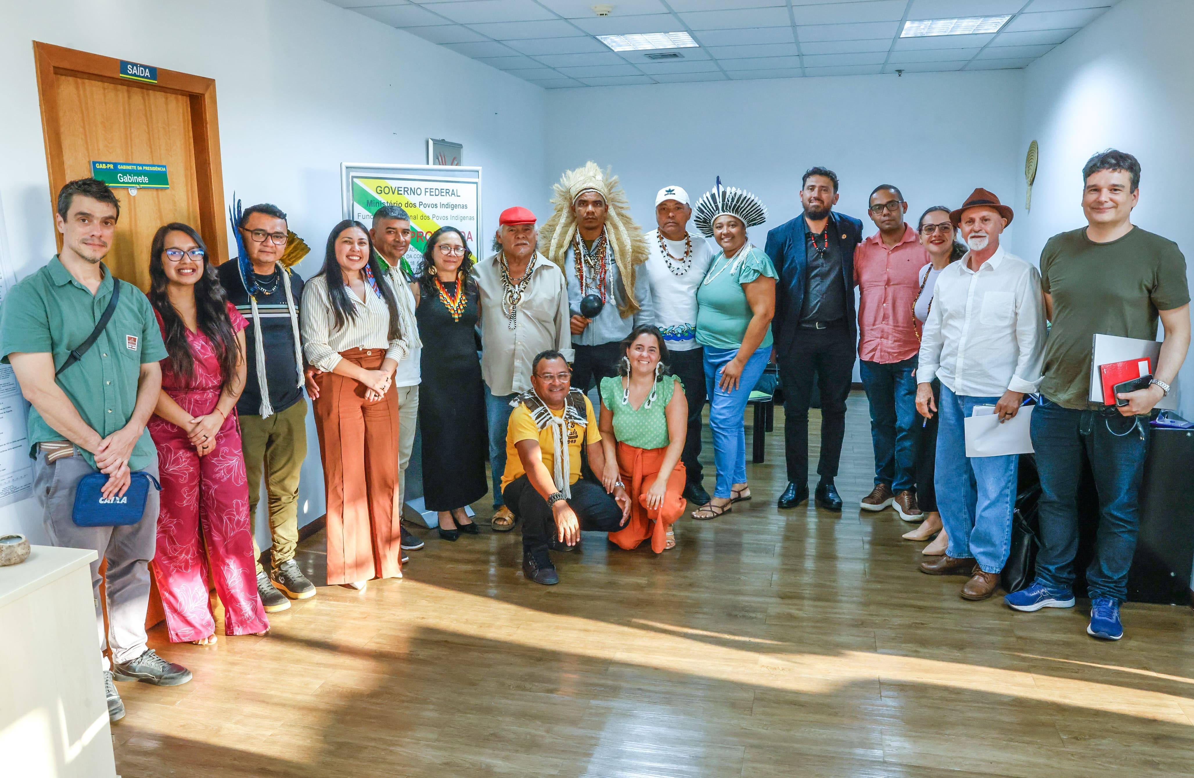 Grupo posa para foto, incluindo homens e mulheres em trajes casuais e lideranças indígenas.