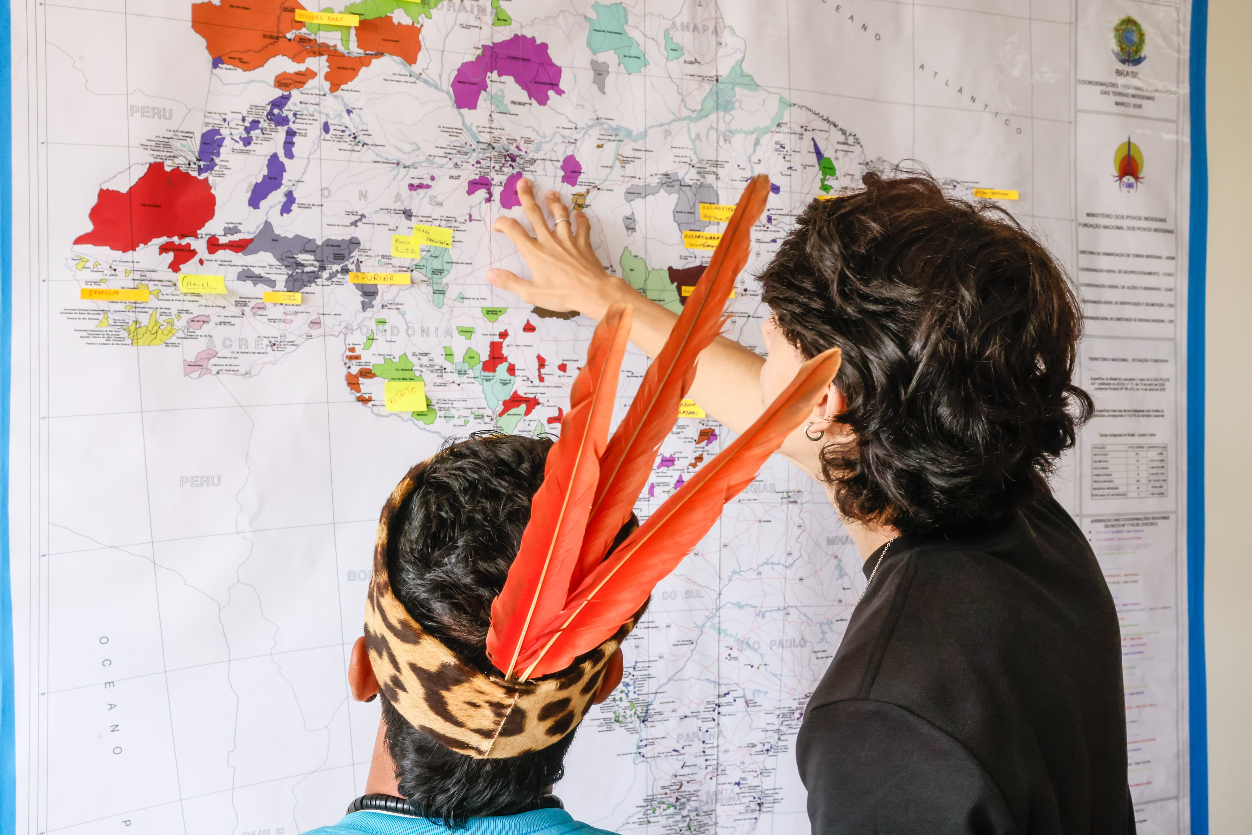 Uma mulher e um indígena na frente de um mapa