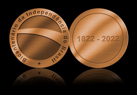 imagem apresenta dois círculos em pé representando a frente e o verso de uma medalha em bronze, fazendo referência à cor da terra. Na frente, um globo central com uma faixa torta simbolizando o centro da bandeira nacional. Nas laterais, as palavras bicentenário da independência do brasil rodeando e uma estrela embaixo terminando o contorno. No verso, um círculo contorna a moeda. Dentro dele as datas 1822 e 2022. 
