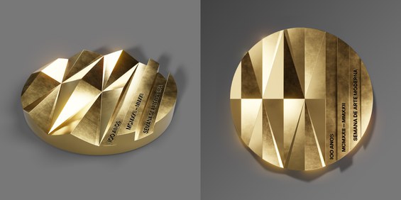 Imagem mostra dois círculos representando a frente e o verso de uma medalha dourada. Na parte da frente, a medalha está deitada. Ela é toda cunhada em relevo de formas geométricas triangulares, formando ondulações. No canto direito, está escrito 100 anos em uma linha; 1922 – 2022, em algarismo romano, em outra linha; e semana de arte moderna em letras maiúsculas, pequenas e pretas em mais uma linha. No verso, a medalha está em pé e é exatamente igual à frente.