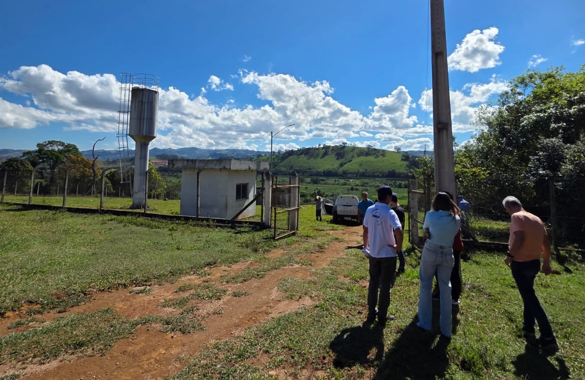 Grupo em área verde observando caixa d'água elevada e edificação em dia ensolarado.