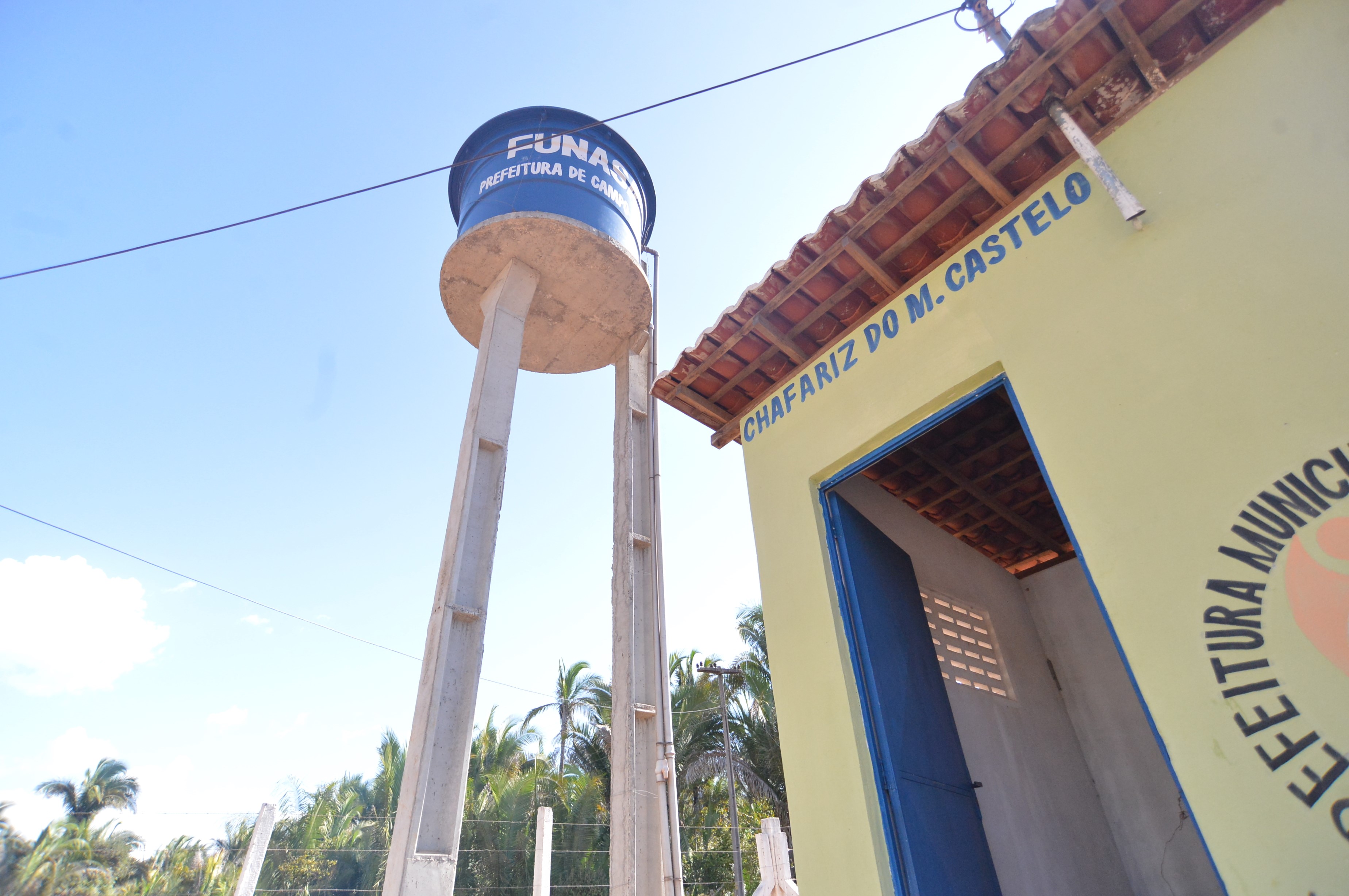 Caixa d'água azul elevada ao lado de estrutura amarela com a frase Chafariz do M. Castelo.