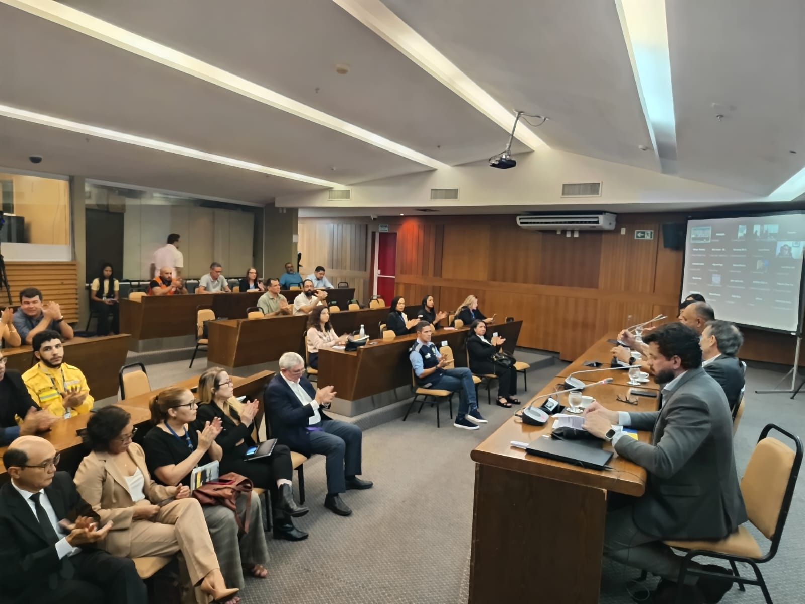 Público no auditório aplaude autoridades durante evento oficial em auditório.