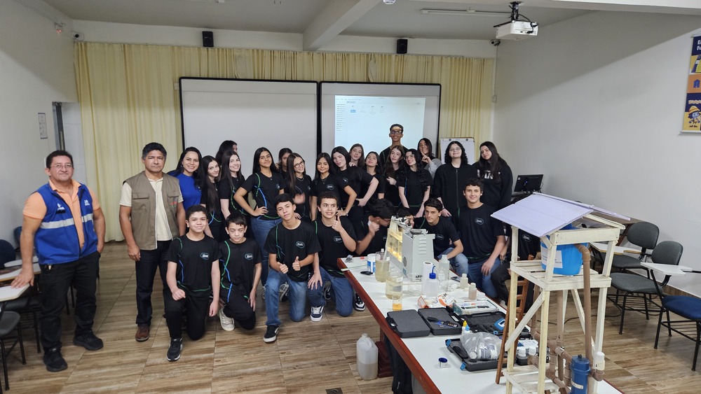 Estudantes e palestrantes em sala de aula ao redor de maquete e equipamentos.
