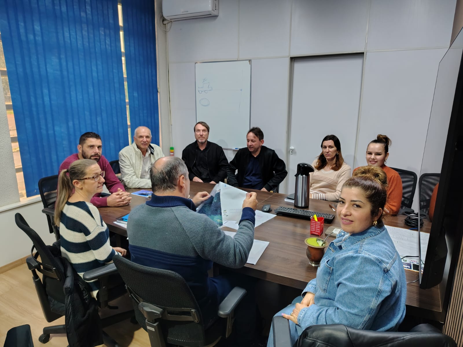 Grupo de pessoas sentado ao redor de uma mesa de reunião em um escritório analisando papéis.