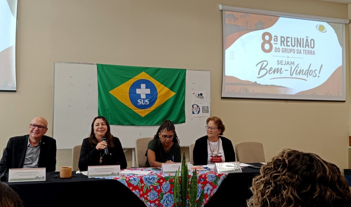 Mesa de debate da Funasa sobre saneamento rural com participantes, bandeira do SUS e tela projetada.