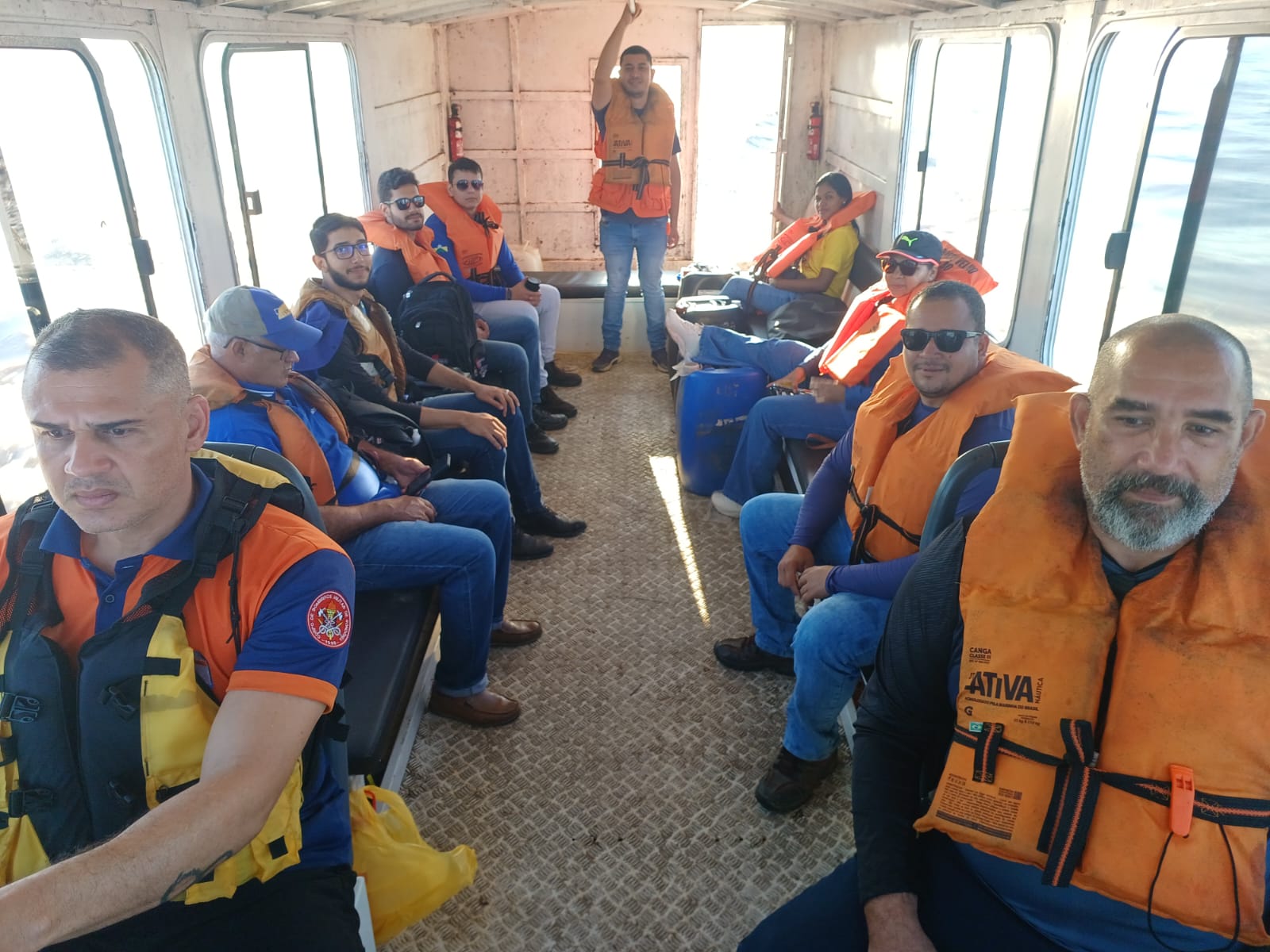 Grupo de pessoas vestindo coletes salva-vidas sentadas no interior de uma embarcação.