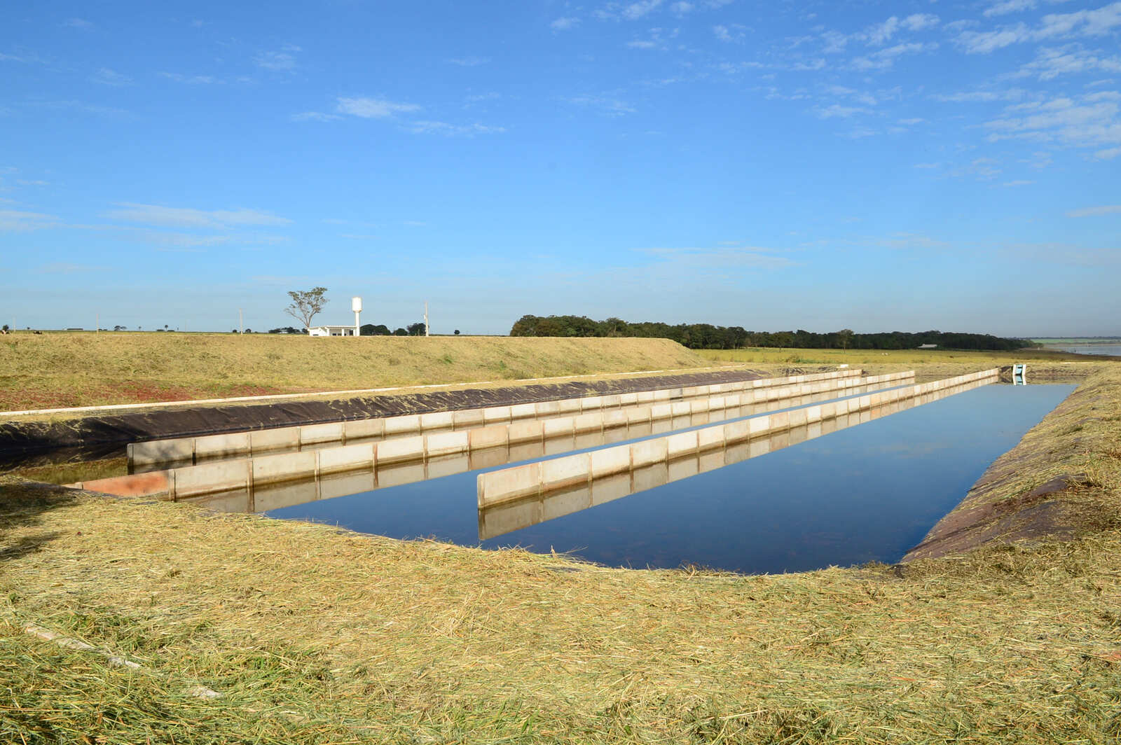 Estação de tratamento de esgoto com lagoas de estabilização paralelas e área gramada.