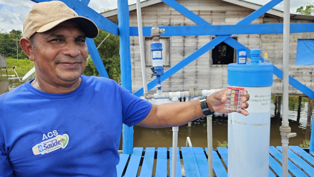 Homem de boné e camiseta azul segura um medidor de teste da água ao lado de um filtro Salta-Z.