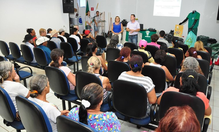 Público assiste a uma palestra em auditório com instrutores ao fundo perto do telão.
