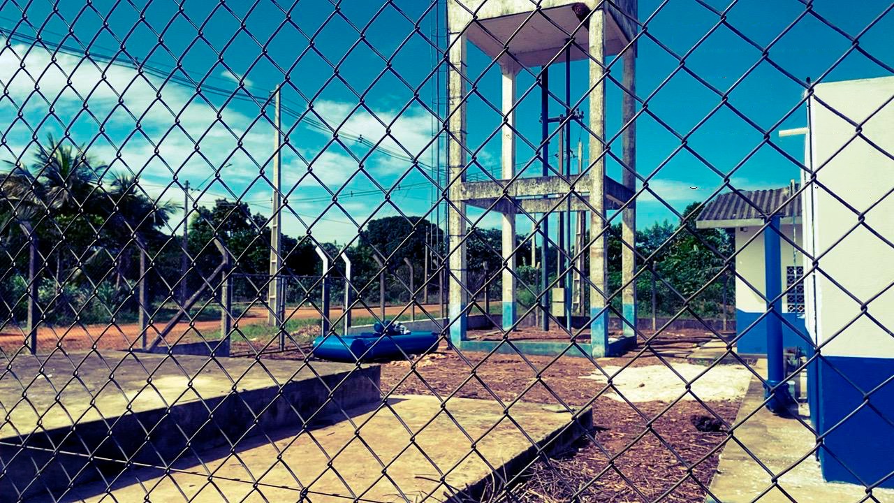 Torre de caixa-d'água de concreto e estruturas do sistema de abastecimento atrás de cerca.
