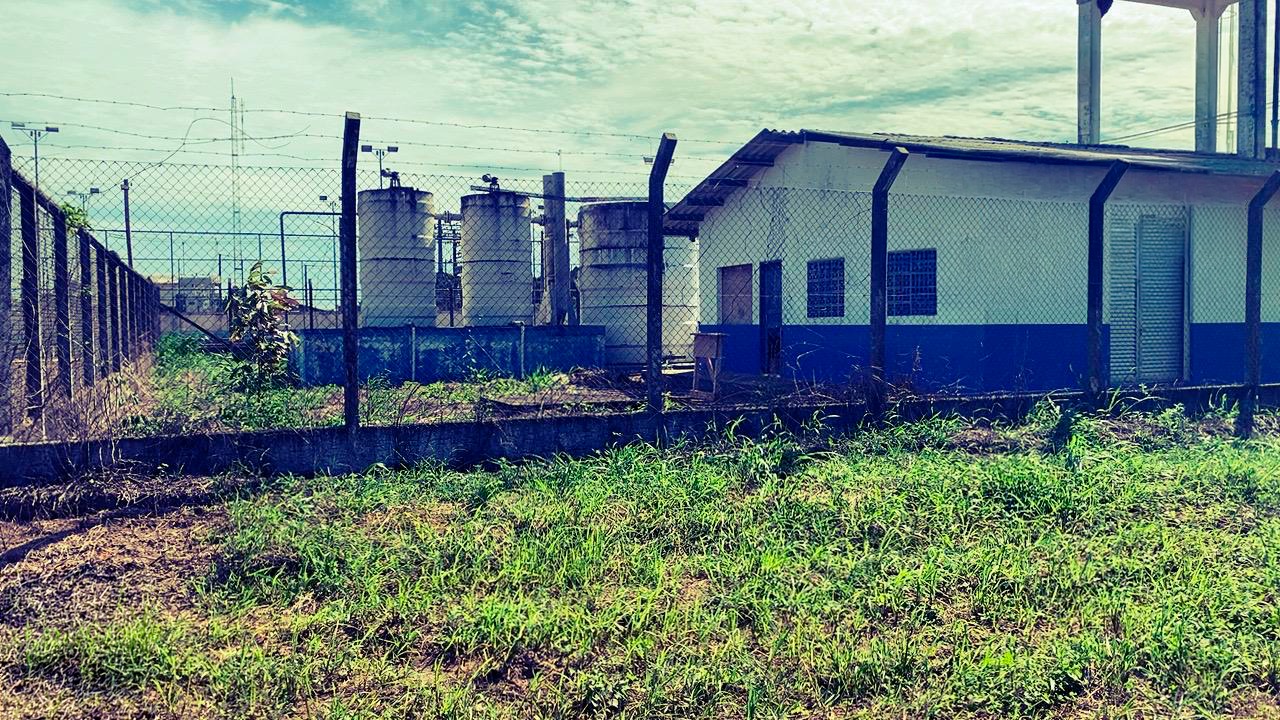 Prédio com detalhes em azul e tanques de água verticais cercados por grade e área verde.