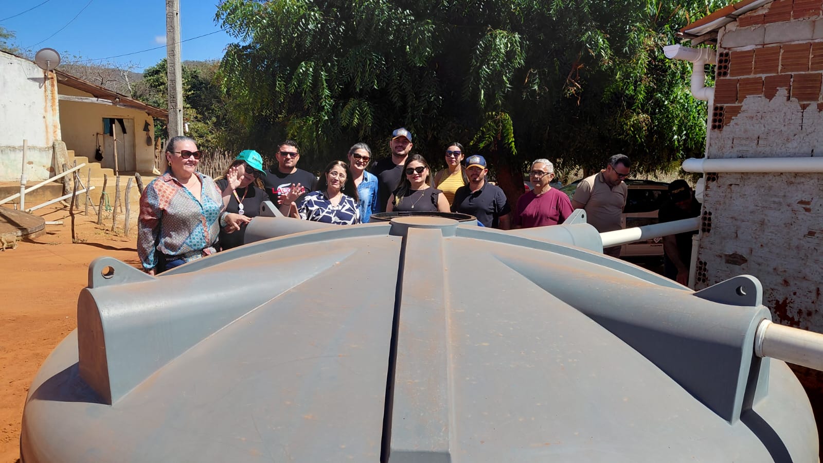 Grupo de pessoas posa reunido atrás de uma grande cisterna cinza em uma área rural.