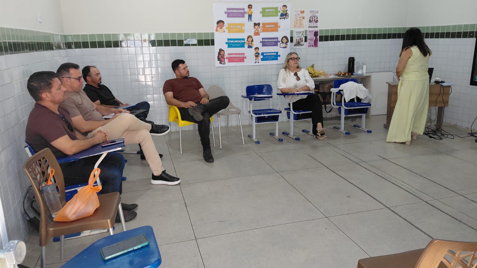 Pessoas sentadas em cadeiras universitárias assistem a uma apresentação em sala de aula.