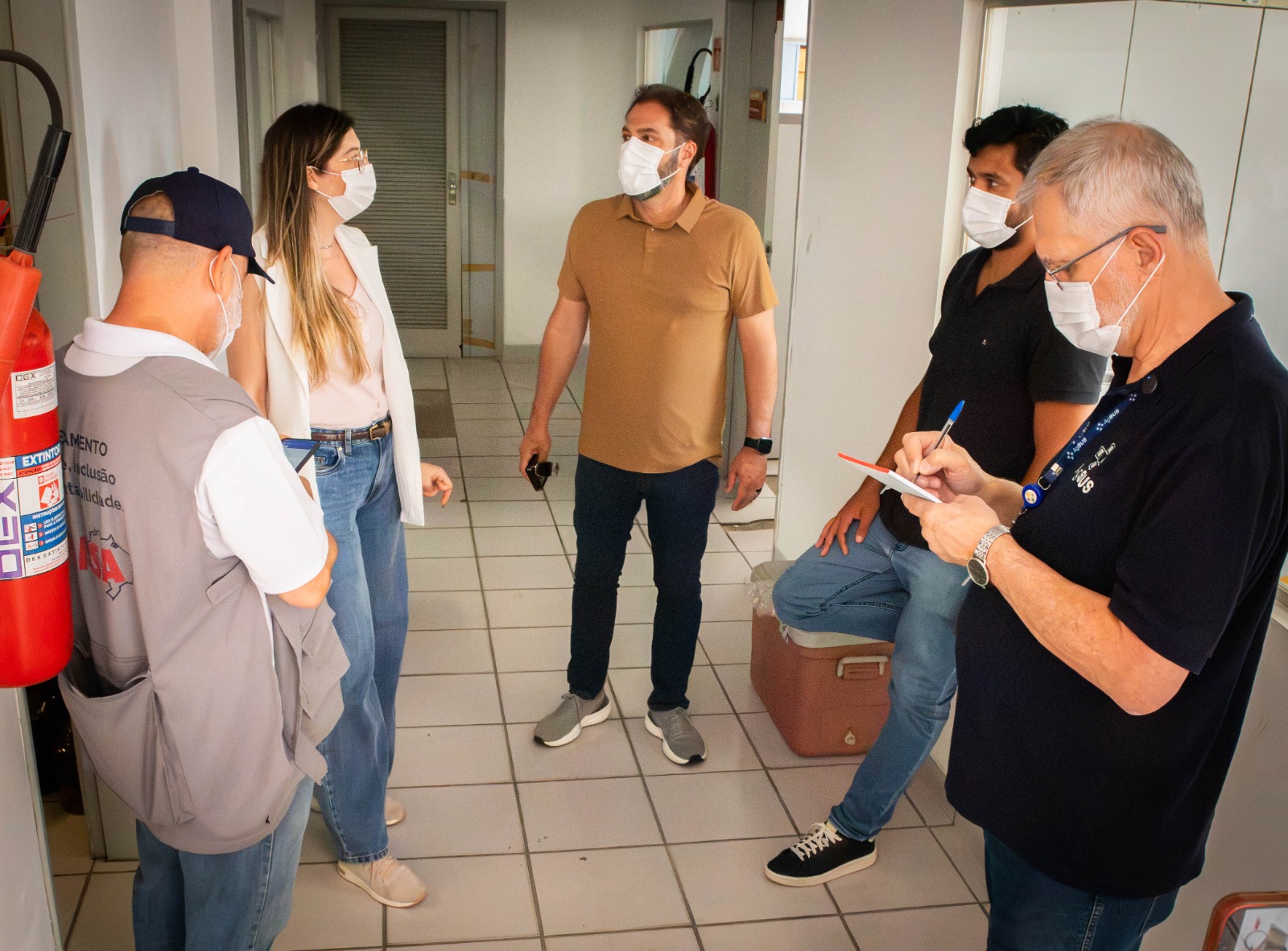 Grupo de pessoas usando máscaras conversa no corredor de um prédio.