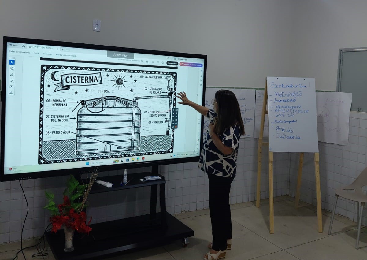 Mulher aponta para tela digital com esquema técnico explicativo sobre funcionamento de cisterna.