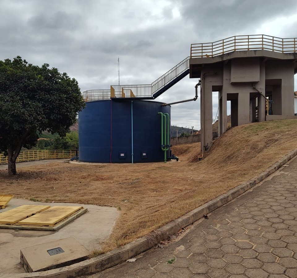 Estação de tratamento com tanque azul, passarelas, estruturas de concreto e pavimento.