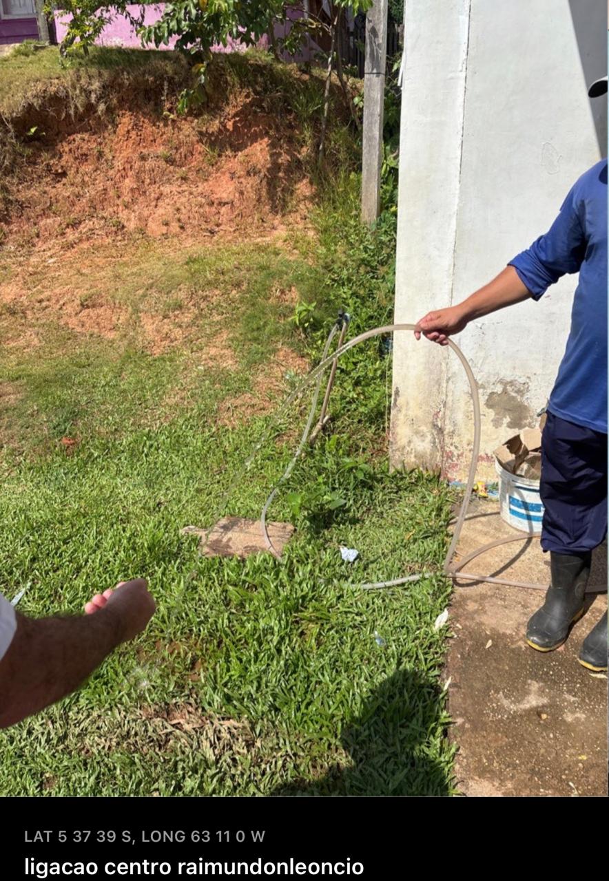 Homem em pé na grama segurando uma mangueira transparente de onde sai água.